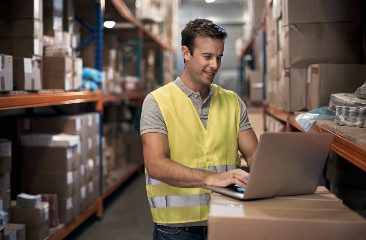 Shot of a young man working on his laptop in a distribution warehouse