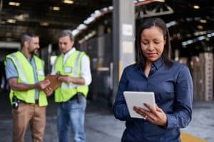 Shot of a warehouse manager holding a digital tablet with workers in the background